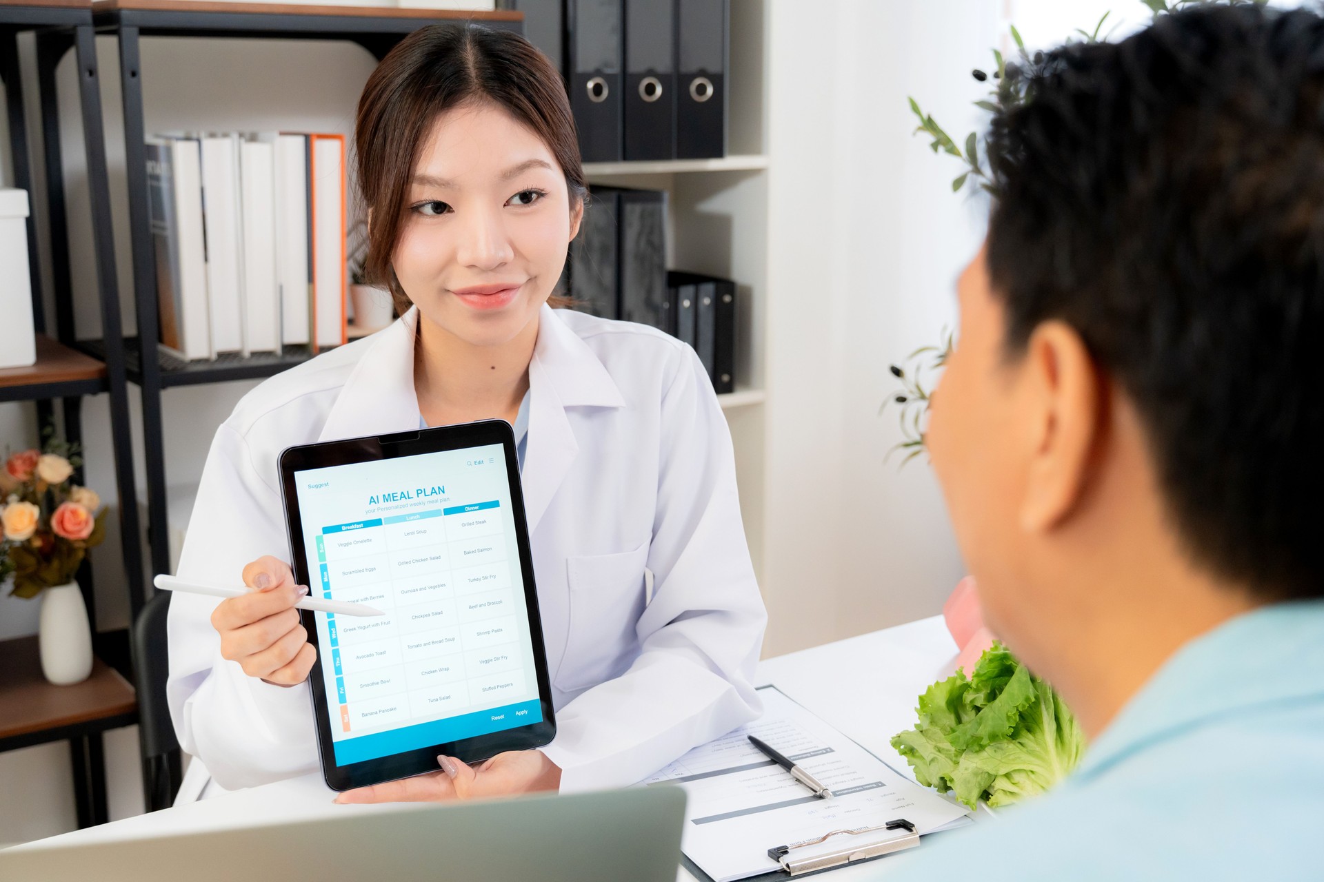 Asian nutritionist using tablet to explaining personalized meal plan with AI to patient during healthcare consultation, healthy lifestyle, woman dietitian showing nutrition plan with AI on tablet.